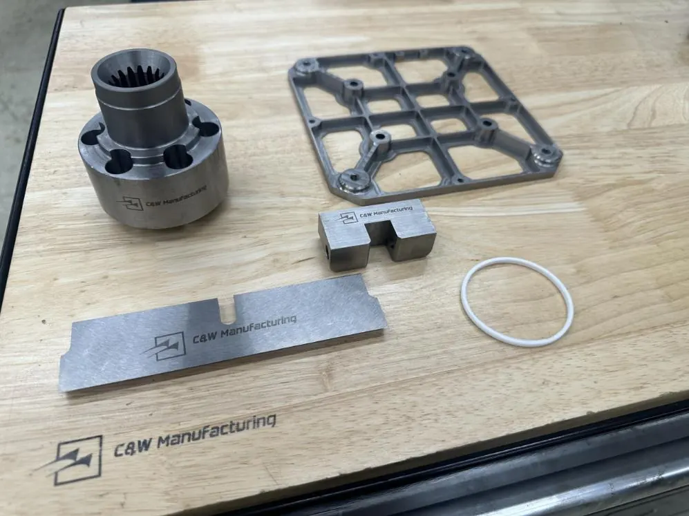 Finished machined sample parts laser-marked with the C&W logo: a splined hub, a grid plate, a slotted block and a ground blade