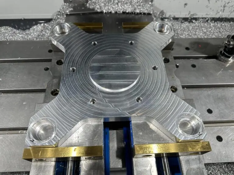 A machined aluminum mounting bracket with four counterbored corner holes and a centre bore